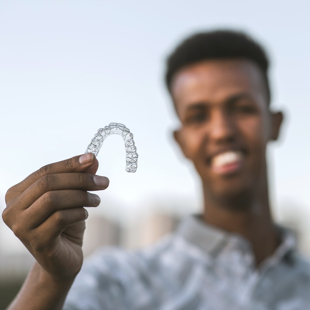 A man with dark skin is holding up a clear aligner tray.