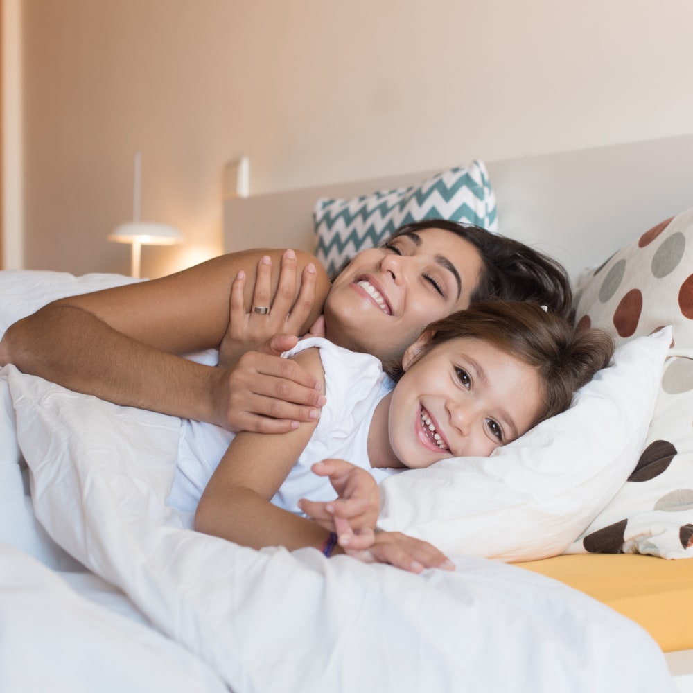 A man is sitting on his bed smiling, seemingly just woken up from a good night's sleep.
